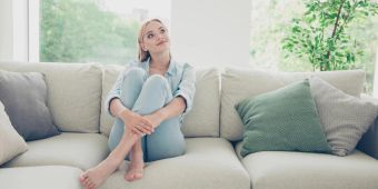 Eine junge Frau sitzt auf dem Sofa und denkt über die Einrichtung ihrer ersten Wohnung nach.