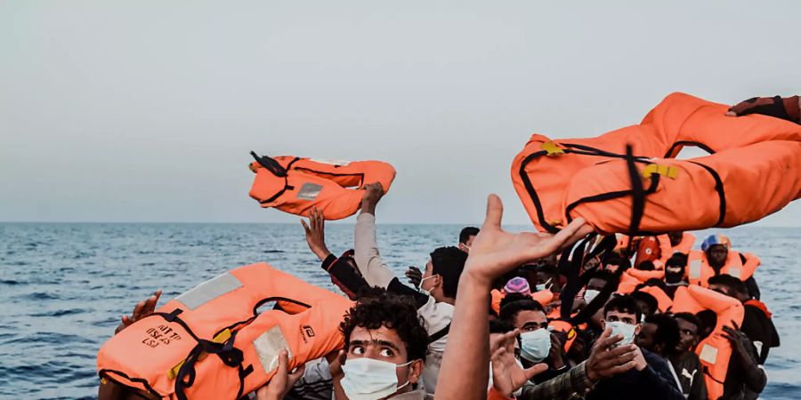 HANDOUT - Ein Helfer reicht den Bootsmigranten in einem kleinen Boot Rettungswesten. Foto: Flavio Gasperini/SOS Mediterranee/dpa - ACHTUNG: Nur zur redaktionellen Verwendung im Zusammenhang mit der aktuellen Berichterstattung und nur mit vollständiger Nennung des vorstehenden Credits