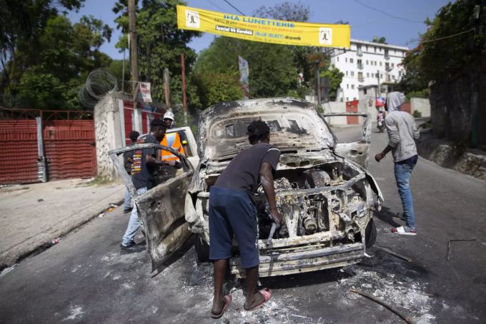 Menschen versuchen Teile vor einem abgebrannten Auto zu retten. Haiti