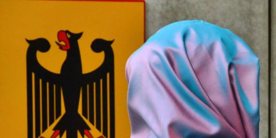 Eine junge Frau mit Kopftuch geht an einem Behördenschild mit dem Bundesadler vorbei. Foto: Martin Schutt/dpa-Zentralbild/dpa/Archivbild
