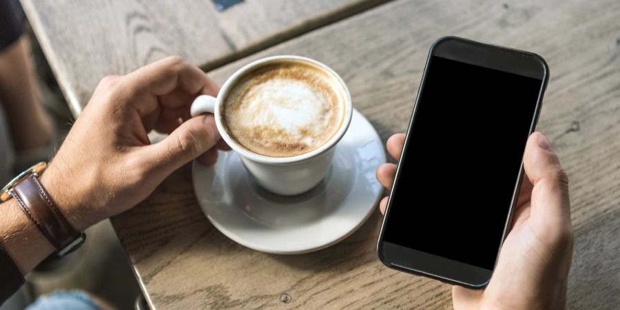 mann schaut auf smartphone, holztisch, kaffee