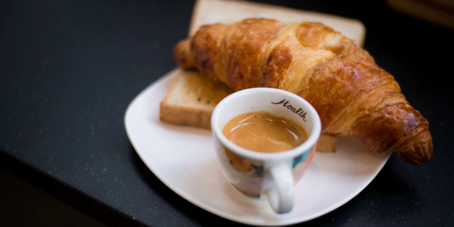 Ein Espresso und ein Croissant auf einem schwarzen Tisch.