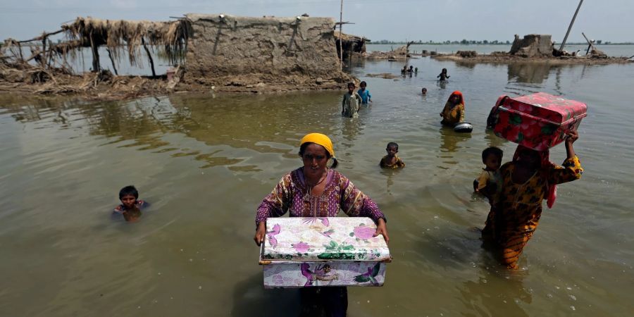 Frauen tragen Habseligkeiten aus ihrem durch heftige Regenfälle überschwemmten Haus im Bezirk Qambar Shahdadkot in der pakistanischen Provinz Sindh.