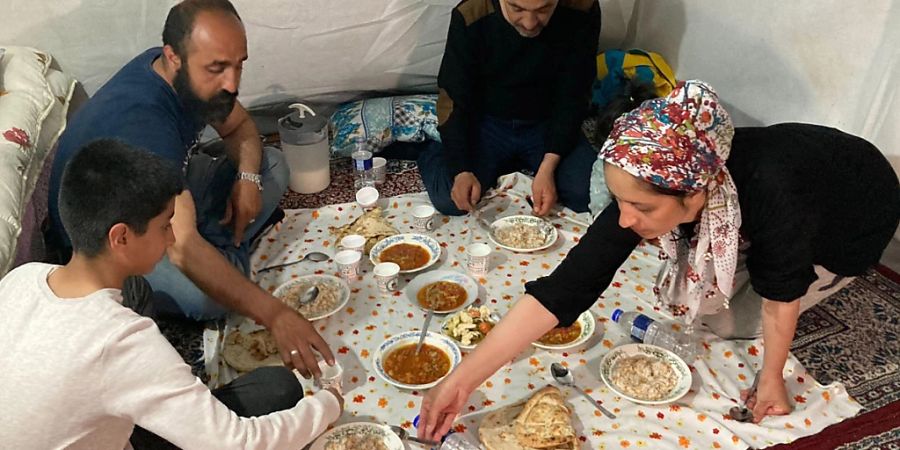Familie Kaplan mit Mutter Asli (r) und ihrem Mann Ekrem (2.v.l) begeht das erste Fastenbrechen in ihrem Zelt. Die Familie lebt seit dem Erdbeben, das den Südosten des Landes schwer traf, in einer Notunterkunft. Foto: Ergin Hava/dpa