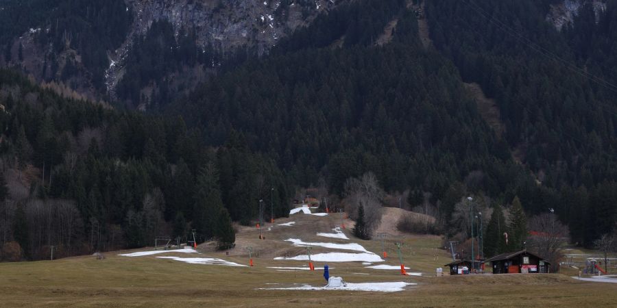 Reste von Kunstschnee auf einer Skipiste in grüner Landschaft.
