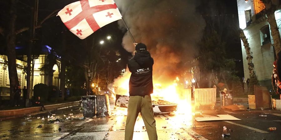 dpatopbilder - Ein Mann schwenkt eine georgische Nationalflagge vor einer brennenden Barrikade in der Nähe des georgischen Parlamentsgebäudes. Foto: Zurab Tsertsvadze/AP