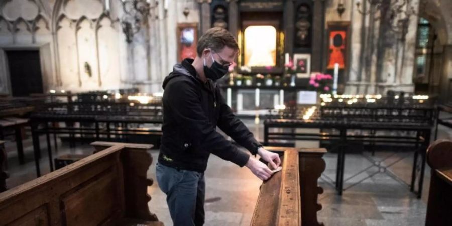 Ein Mitarbeiter der Dombauhütte klebt Aufkleber auf Kirchenbänke im Kölner Dom. Die runden Sticker sollen den Platz markieren, auf den Gottesdienstbesucher sich setzen dürfen. Foto: Federico Gambarini/dpa
