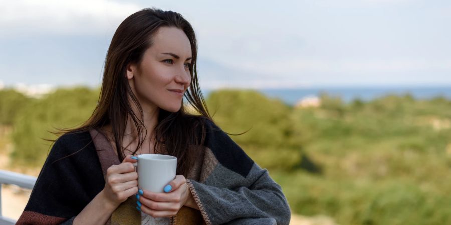 Eine Frau auf einem Balkon mit einer Tasse in ihrer Hand.