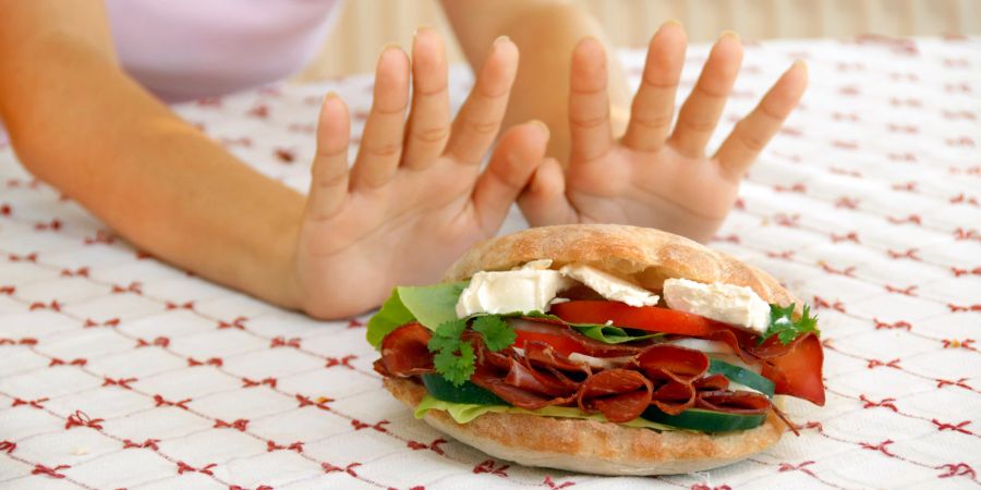 frauenhände halten sandwich von sich weg, rote tischdecke