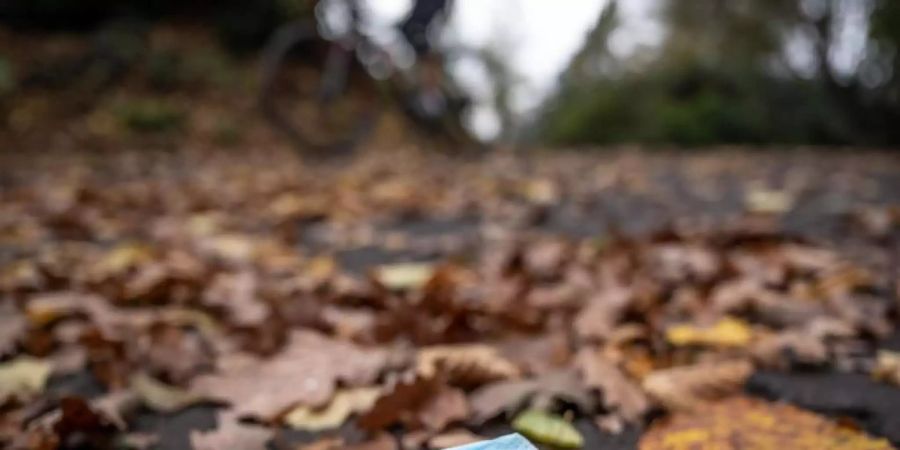 Eine weggeworfene Maske zwischen Herbstlaub auf einer Strasse. Foto: Bernd Thissen/dpa