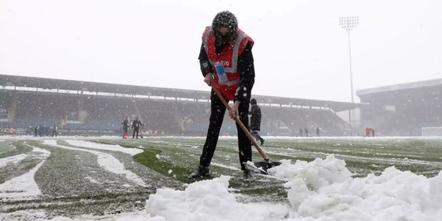 Der Rasen im Staion Turf Moor ist nicht bespielbar: Mitarbeiter räumen den Schnee vom Spielfeld. Foto: Bradley Collyer/PA Wire/dpa