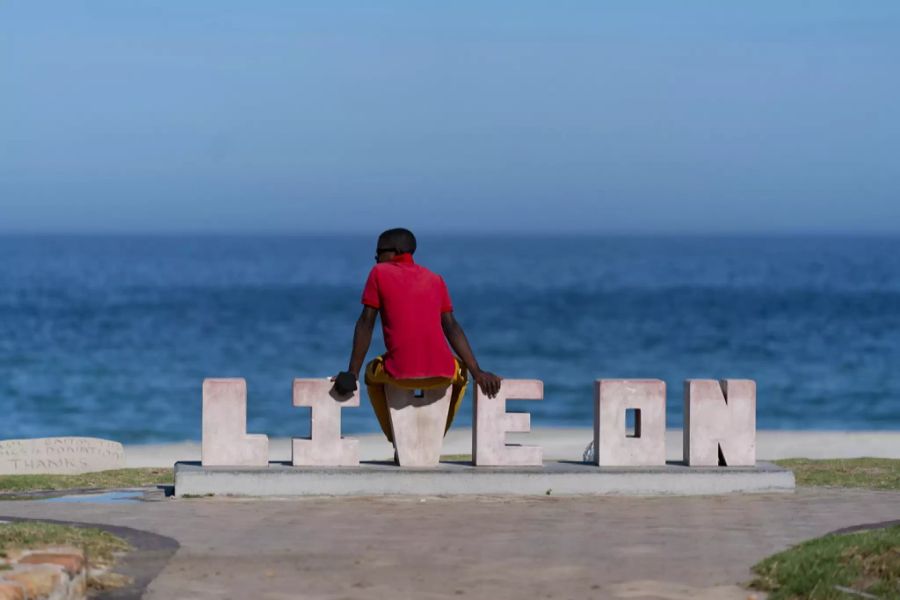 Südafrika im Lockdown: Ein Mann sitzt auf einer Skulptur mit dem Schriftzug «Live on» (lebe weiter) am geschlossenen Strand der Blue Flagged Camps Bay in Kapstadt, am 21. Januar 2021.