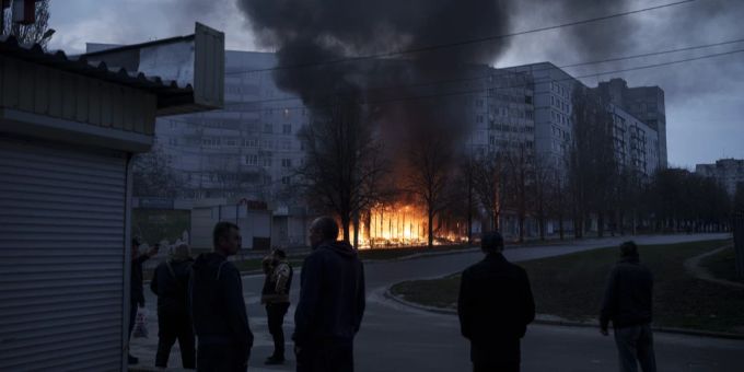 Zivilisten stehen vor einem brennenden Wohnhaus in Charkiw. ukraine Krieg