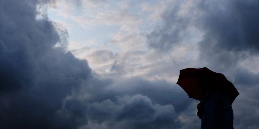 Ein Mann geht mit einem Regenschirm vor aufziehenden dunklen Wolken in Duisburg spazieren. (Symbolbild)
