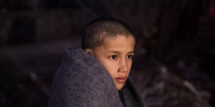 Ein Junge sitzt in Decken eingewickelt am Strand des Dorfes Skala Sikamias, nachdem er mit einem Beiboot die Ägäis von der Türkei aus überquert hat. Foto: Angelos Tzortzinis/dpa