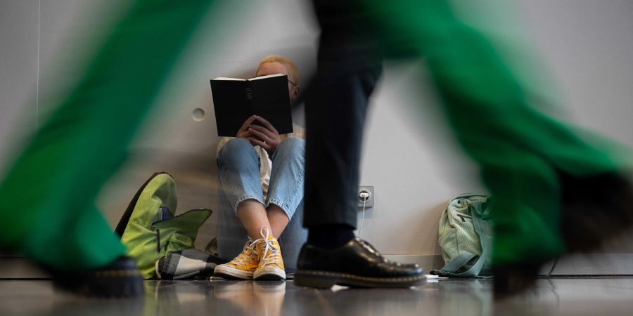 Eine Frau sitzt während der Frankfurter Buchmesse lesend an einer Wand hinter Messebesuchern.