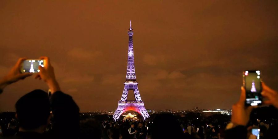 Touristen fotografieren den Eiffelturm, der im Rahmen des Besuchs des japanischen Kronprinzen Naruhito in Frankreich beleuchtet wurde.