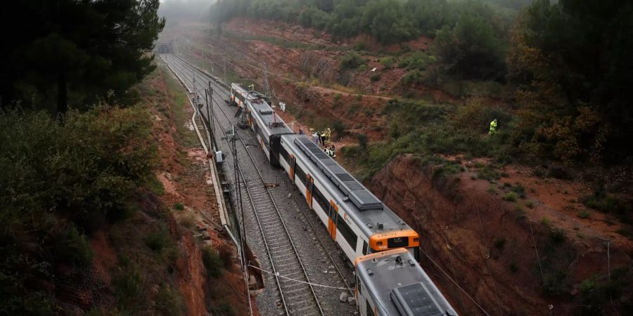 Feuerwehrleute und Rettungskräfte stehen in der Nähe von Barcelona (ESP) an den entgleisten Wagen eines Nahverkehrszugs.