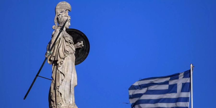 Eine Staute der Athene, griechische Göttin der Weisheit, der Strategie und des Kampfes, steht neben einer griechischen Flagge in Athen.