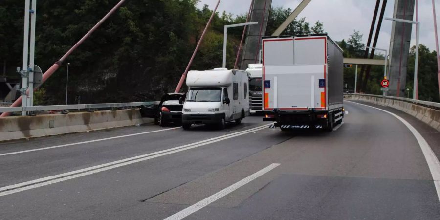 Verunfalltes schwarzes Auto, weisses Wohnmobil und weisser Lastwagen auf Schrägseilbrücke - Keystone