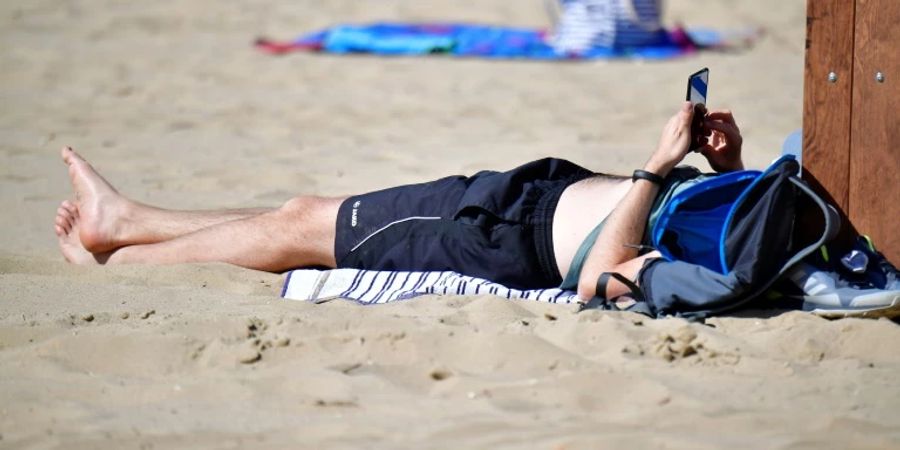 Mann mit Handy an einem Strand.