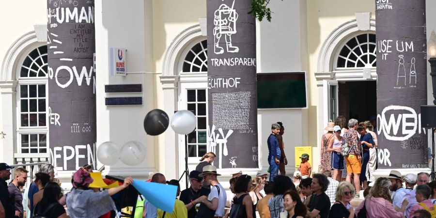 Besucher der documenta fifteen stehen nach Eröffnung vor dem Fridericianum, dessen Säulen der rumänische Künstler Dan Perjovschi mit schwarzer Farbe bemalt und mit weissen Symbolen und Zeichen zu Themen wie Frieden, Solidarität oder Nachhaltigkeit beschriftet hat.