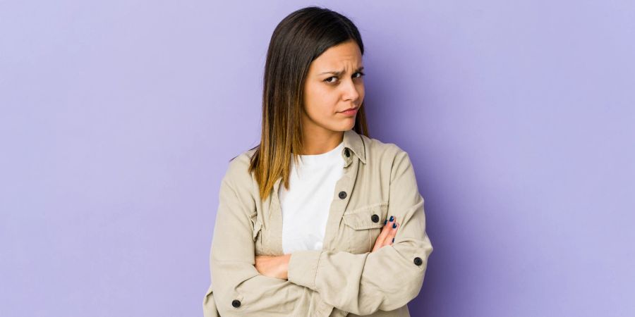 frau schaut verdächtigend, mit verschränkten armen, lila hintergrund