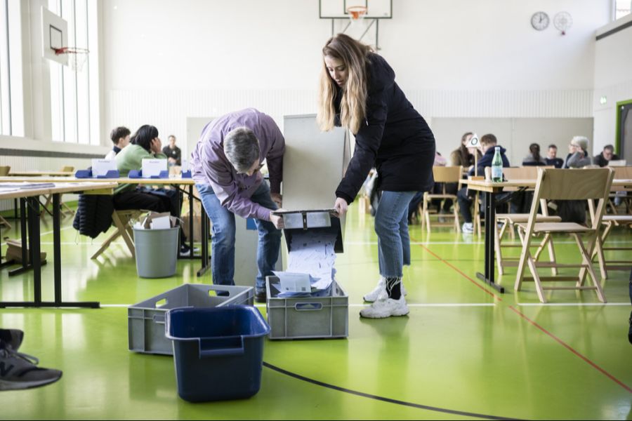 Freiwillige Mitarbeiter helfen beim Ausleeren der Urne mit den Abstimmungsunterlagen zu den Regierungs- und Kantonsratswahlen 2023 im Schulhaus Aemtler, am 12. Februar 2023 in Zürich.