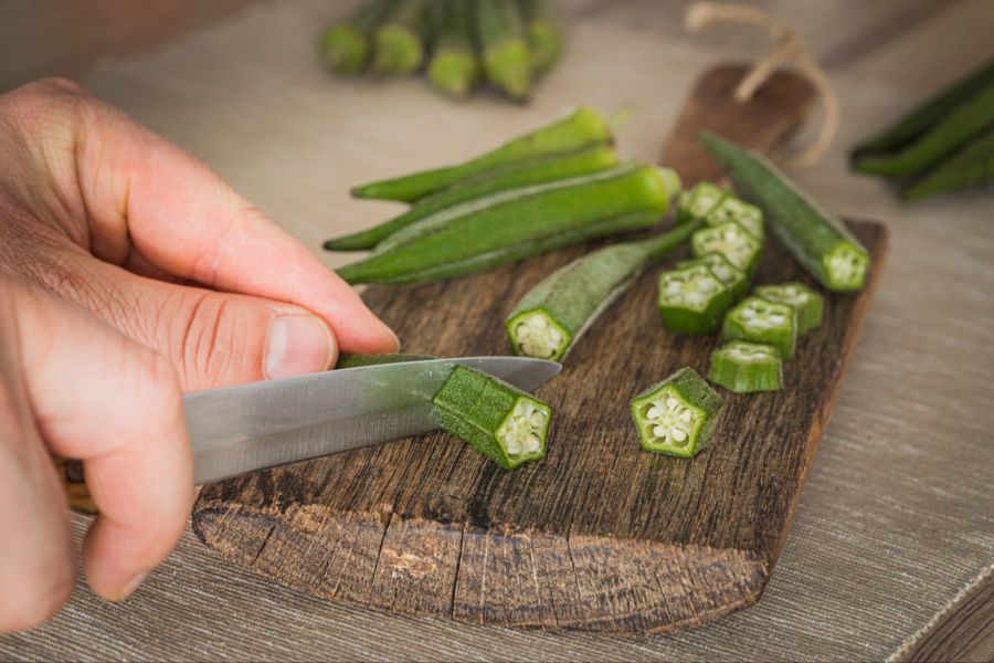 Person schneidet Okra auf einem Brett