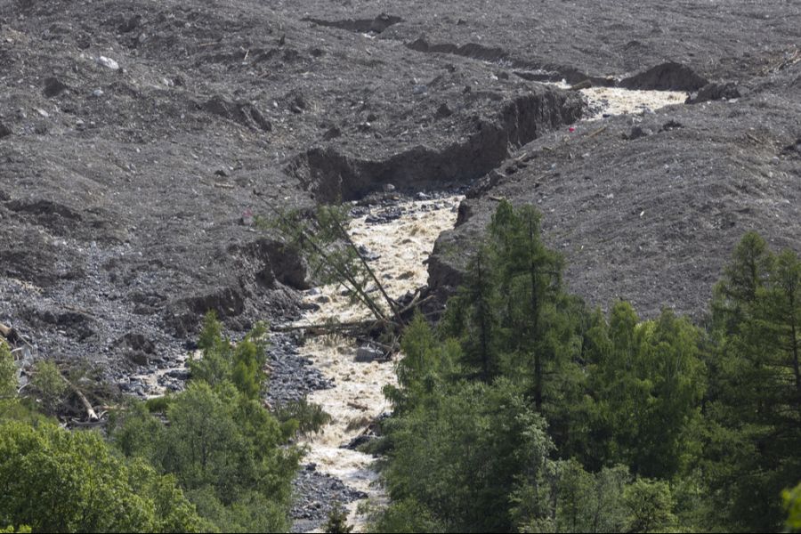 Wasser der Lonza fliesst über Schlamm und Geröll an den letzten Häusern von Blatten vorbei.