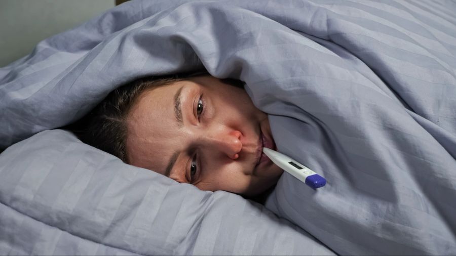 Frau erkältet im Bett mit Fieberthermometer