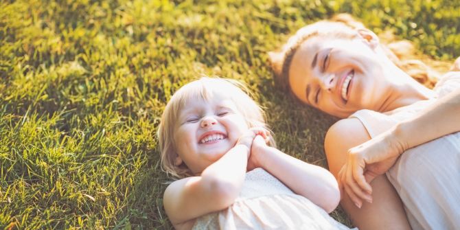 mutter und kind liegen auf wiese und lachen gemeinsam