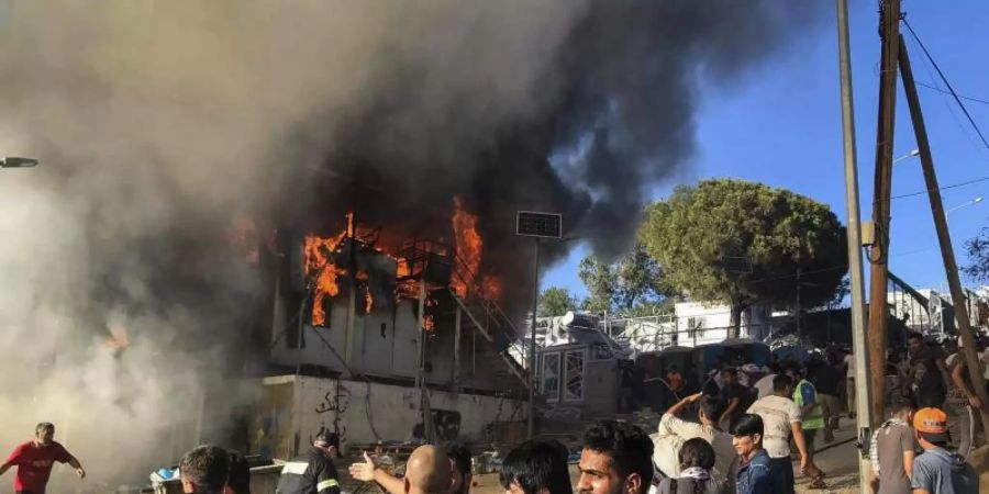 Migranten und Flüchtlinge stehen neben brennenden Hauscontainern. Foto: InTime News/AP