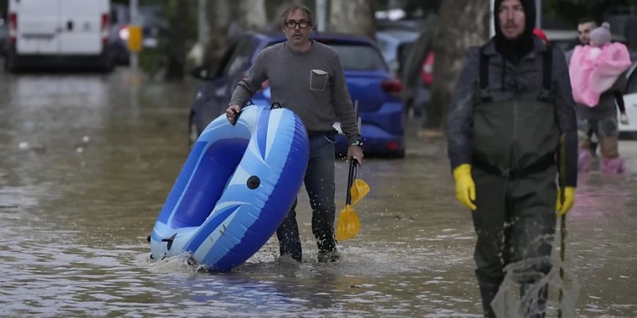 Menschen bahnen sich ihren Weg auf einer überfluteten Strasse in der mittelitalienischen Region Toskana. Foto: Gregorio Borgia/AP/dpa