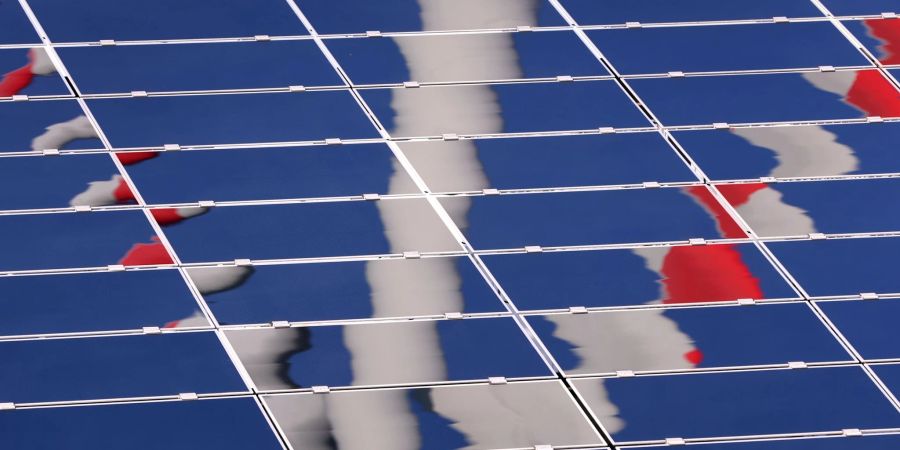 Ein Windrad spiegelt sich in eine Photovoltaik-Anlage eines Solarparks.