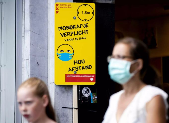 Eine Frau mit Mundschutz geht an einem Schild mit Informationen über die Maskenpflicht vorbei. Das Tragen eines Mund-Nasen-Schutzes aufgrund des Coronavirus ist an belebten Orten in Amsterdam Pflicht. Coronavirus - Niederlande