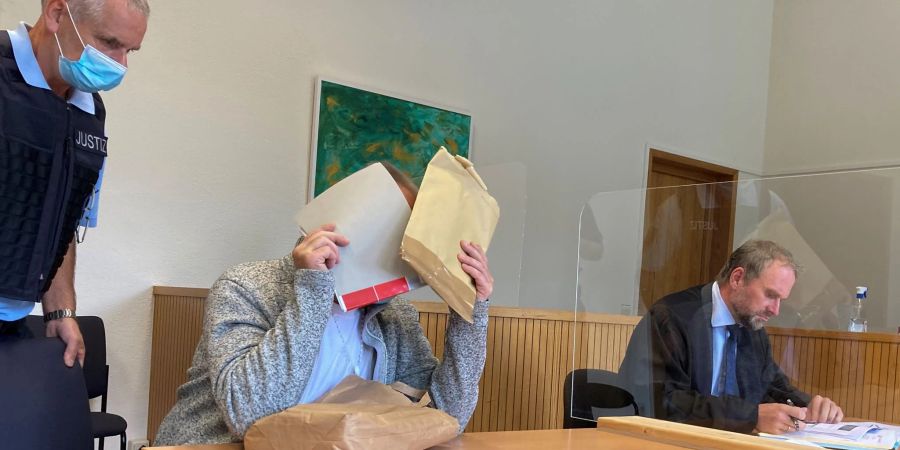 Der Angeklagte im sogenannten Cophunter-Prozess sitzt im Gerichtssaal des Amtsgerichts Idar-Oberstein und hält sich Akten vor sein Gesicht.