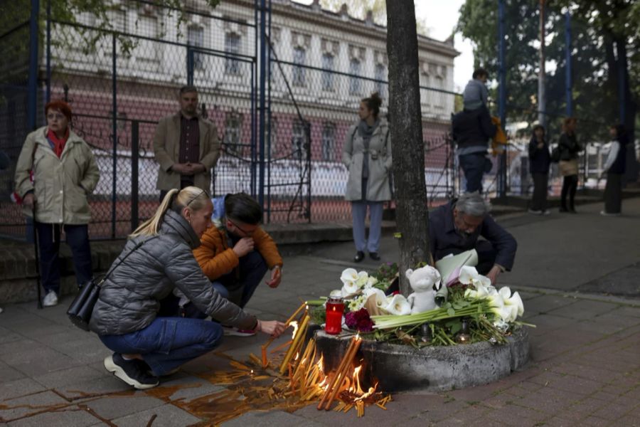 Menschen legen Blumen nieder und zünden Kerzen an vor dem Schulgelände in Belgrad.