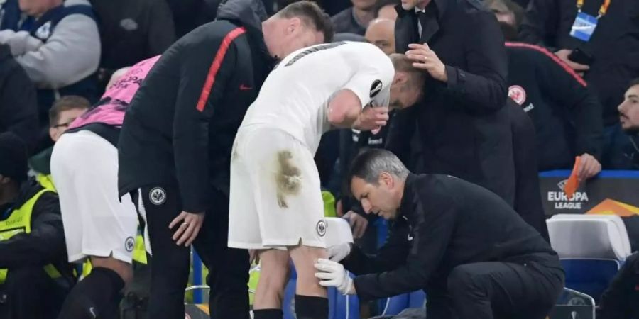 Sebastian Rode (M) wird neben Trainer Adi Hütter (2.v.r.) bei Spiel gegen Chelsea am Knie behandelt. Foto: Arne Dedert