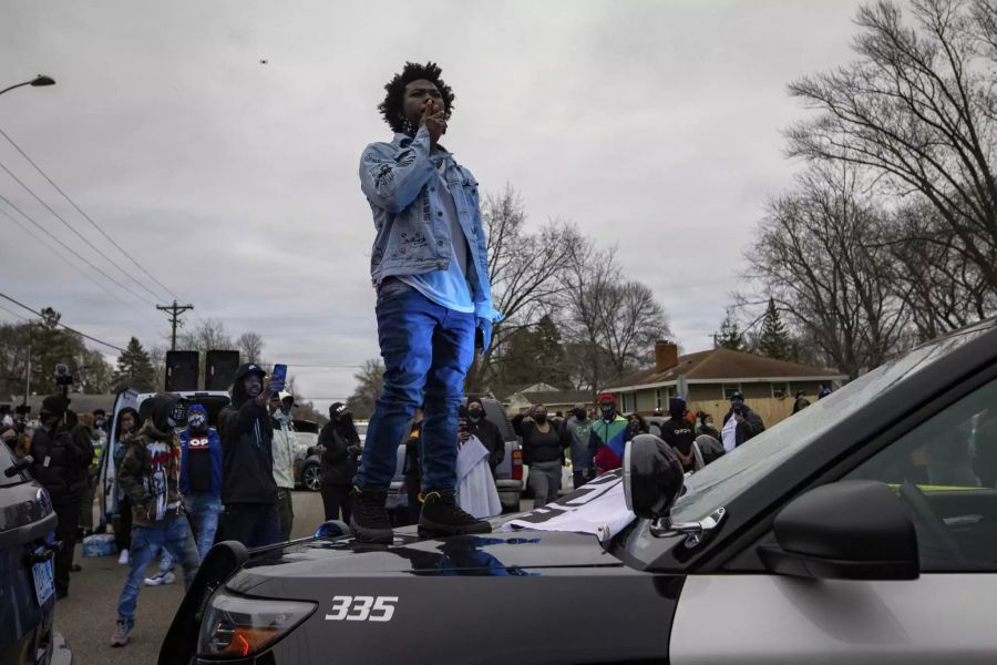 Ein Demonstrant raucht, während er auf der Motorhaube eines Polizeiautos steht, am Sonntag, 11. April 2021, in Brooklyn Center, Minn. (USA)