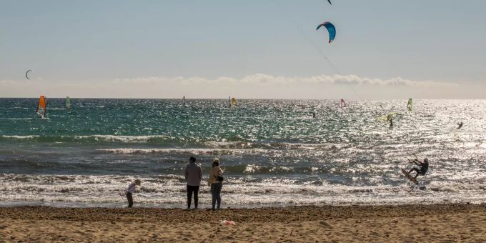 Eine Familie spaziert am Strand, während Kitesurfer den Tag das Meer vor Can Pastilla geniessen. Coronavirus - Mallorca