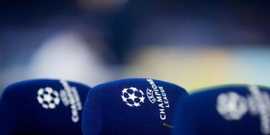 Mikrofone mit dem Logo der Champions League liegen vor einem Spiel auf einem Tisch. Foto: Rolf Vennenbernd/dpa