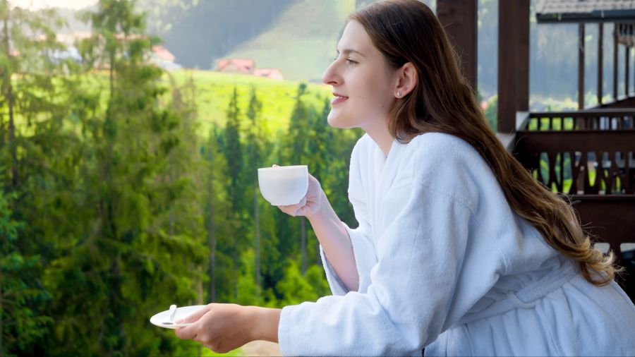 Frau im Bademantel trinkt Kaffee auf Balkon