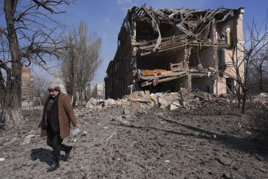 Eine Frau geht an einem durch Beschuss beschädigten Gebäude in Mariupol, Ukraine, vorbei, Sonntag, 13. März 2022.