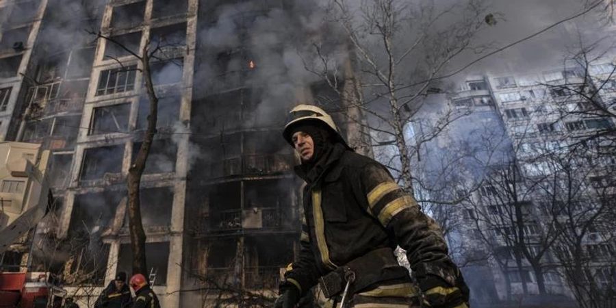 Einsatzkräfte der Feuerwehr stehen in Kiew vor einem brennenden Wohngebäude, dass durch Bombenbeschuss des russischen Militärs zerstört wurde. Foto: Vadim Ghirda/AP/dpa