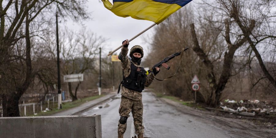 Ein ukrainischer Soldat steht an einer Strassenblockade und hält die ukrainische Flagge hoch.