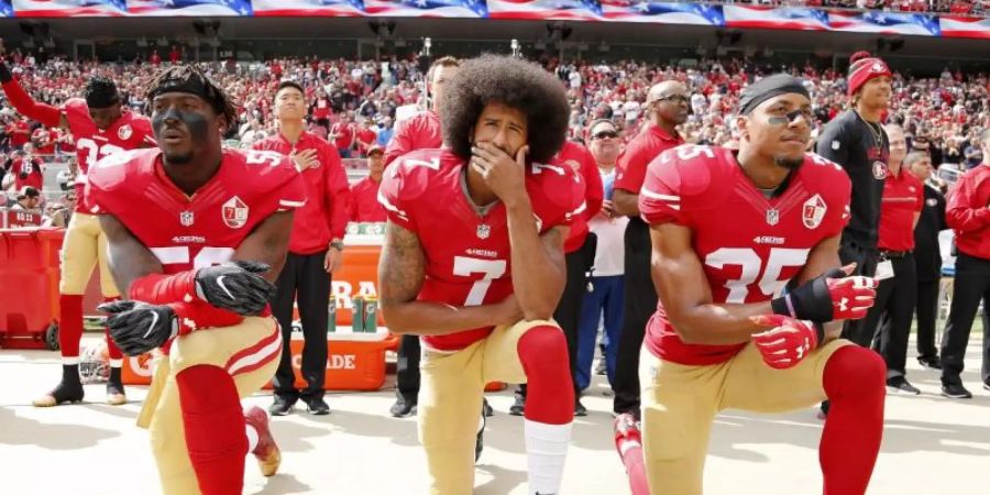 Colin Kaepernick (M), Eli Harold (l) und Eric Reid von den San Francisco 49ers knien 2016 beim Abspielen der US-Nationalhymne. Foto: John G Mabanglo/EPA/dpa