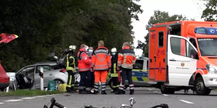 Der zerbrochene Rahmen eines Rennrads liegt an der Unfallstelle in Lienen. Im Hintergrund stehen Einsatzkräfte von Feuerwehr und Rettungsdienst. Foto: -/Nord-West-Media TV/dpa