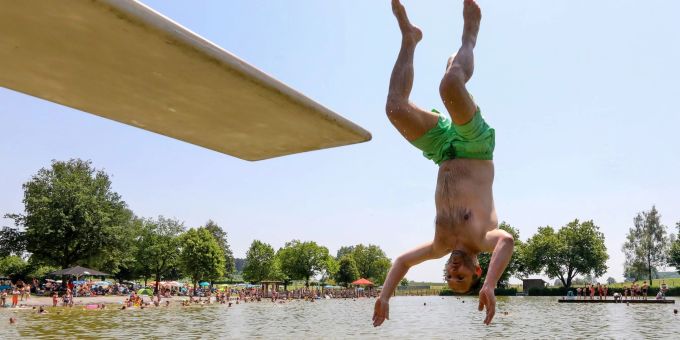 Ein Mann springt kopfüber von einem Sprungbrett in das Wasser. Wasser Hitze