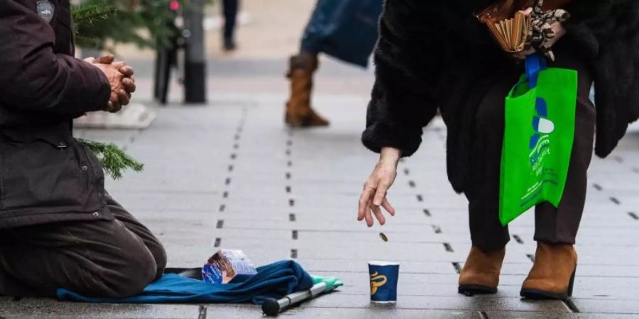 Eine Frau wirft einem Bettler in einer Einkaufsstrasse ein Geldstück in einen Becher. Foto: Andreas Arnold/dpa